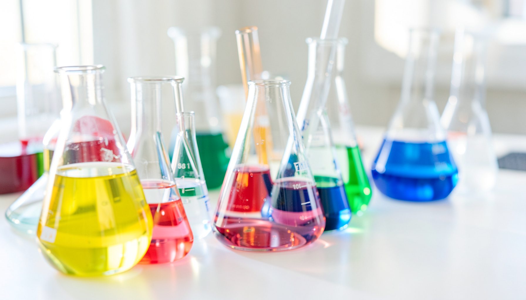 A close-up of colorful laboratory glassware on a bright white table, soft natural light, clean and curious mood